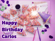 Happy Birthday Carlos GIF: A big paper sparkle highlights this animated birthday gif showing a birthday cake place setting with decorations.